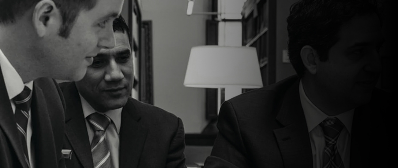 A group of three men in formal suits gathered at a table